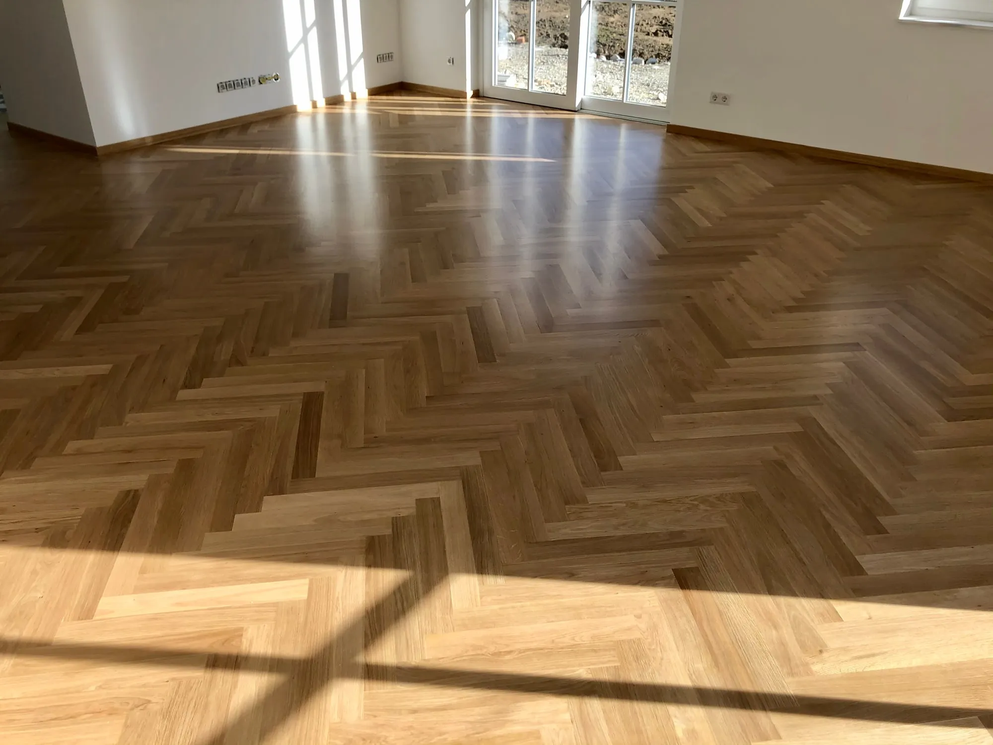 Fischgrätparkett aus Eiche im Sonnenlicht vor einer Fensterfront