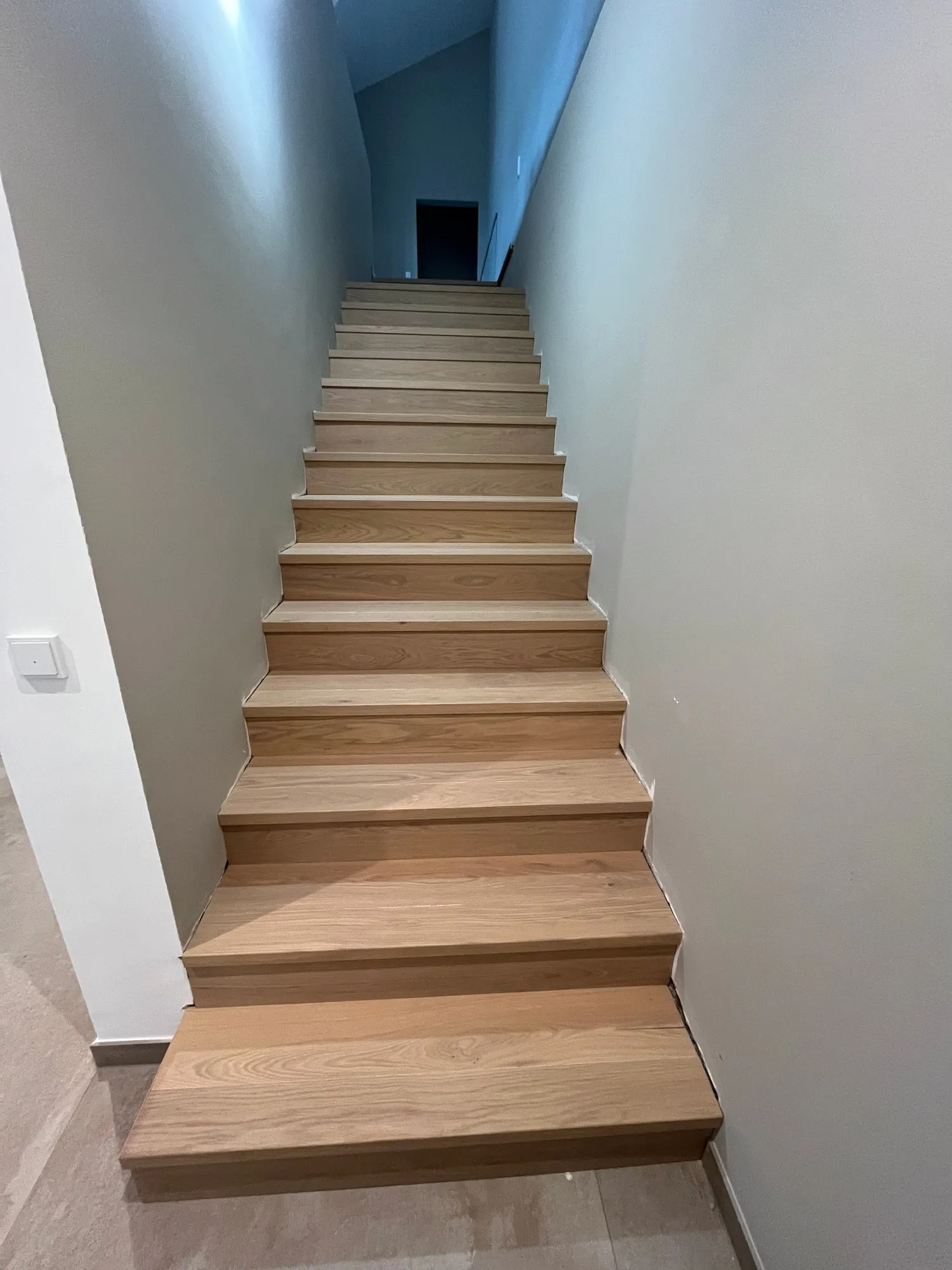 Gerade Treppe mit Stufen aus Eiche zwischen weißen Wänden