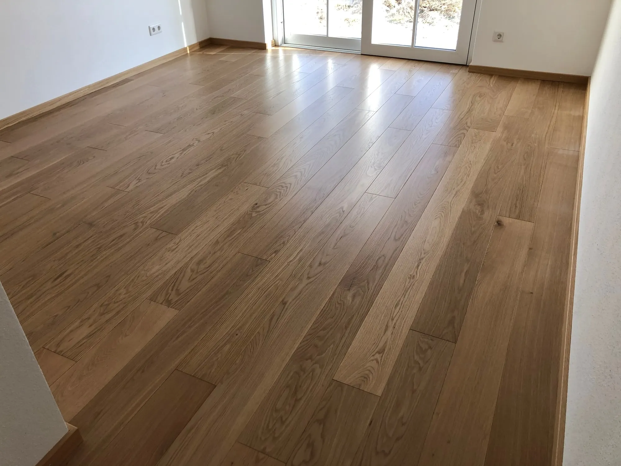 Leerer Raum mit Dielenboden aus Eiche und passenden Sockelleisten, im Hintergrund eine Fenstertür
